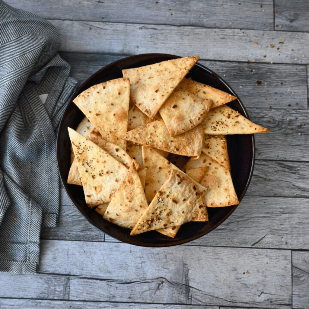 Crispy air fried tortilla chips in a black bowl on a wooden table with a gray cloth.