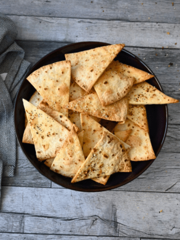 Crispy air fried tortilla chips in a black bowl on a wooden table with a gray cloth.