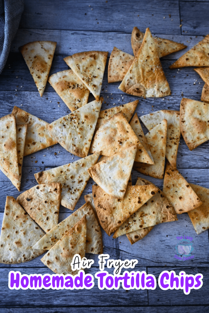 Golden-brown homemade air fryer pita chips, cut into triangles and seasoned, are spread out on a rustic wooden table.