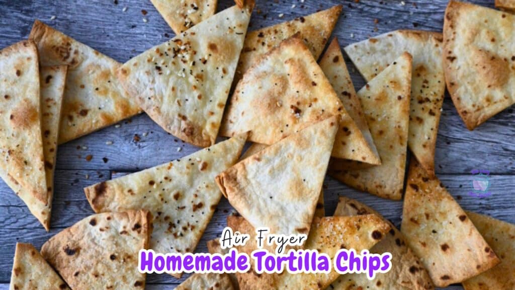 Golden-brown homemade air fryer pita chips, cut into triangles and seasoned, are spread out on a rustic wooden table.