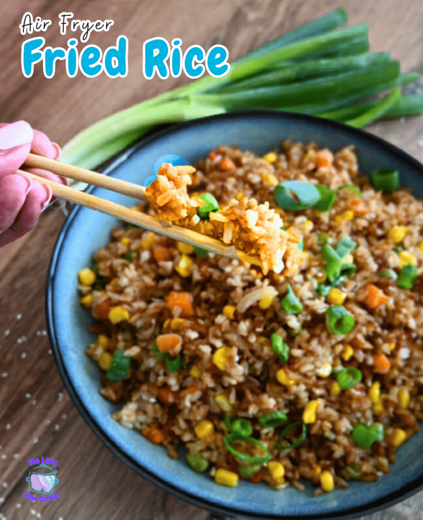 Chopsticks lift a serving of air fryer fried rice with corn, carrots, and green onions from a bowl; green onions in the background.