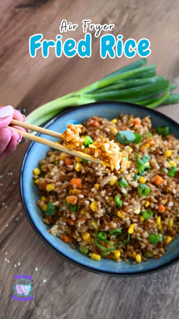 A hand with chopsticks lifts a bite of fried rice with corn, peas, and carrots from a bowl. Text above says Air Fryer Fried Rice.