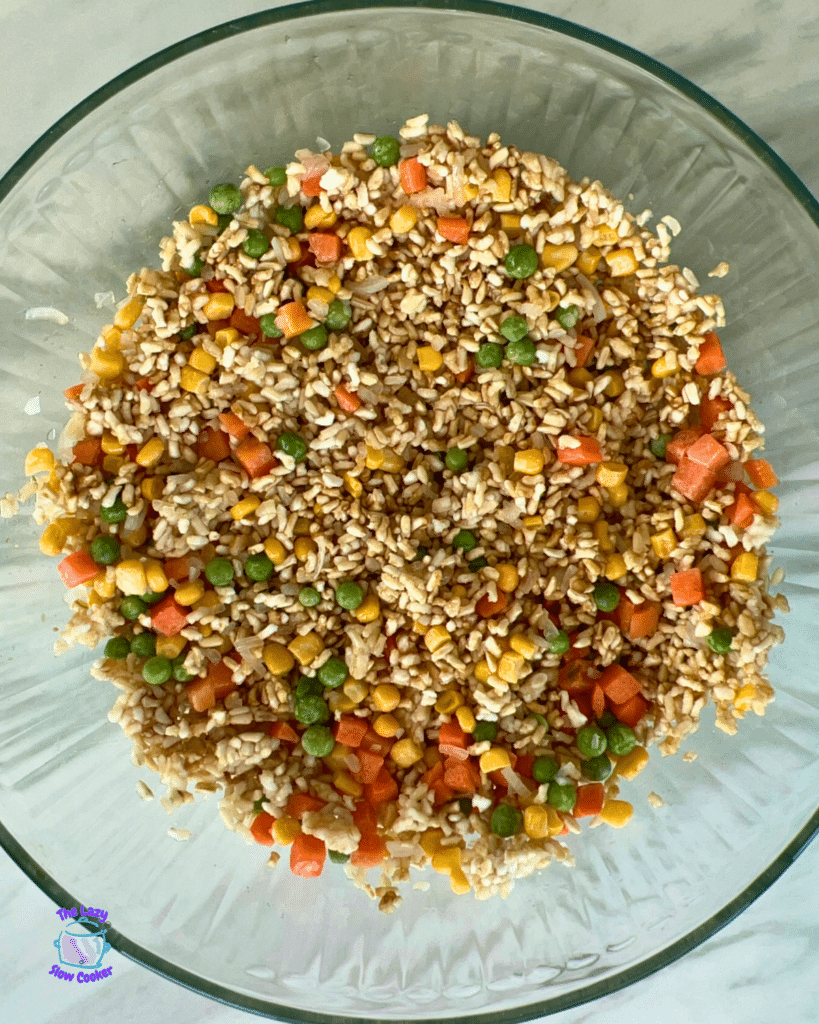 A glass bowl of air fryer fried rice with peas, corn, and diced carrots rests on a pale surface.