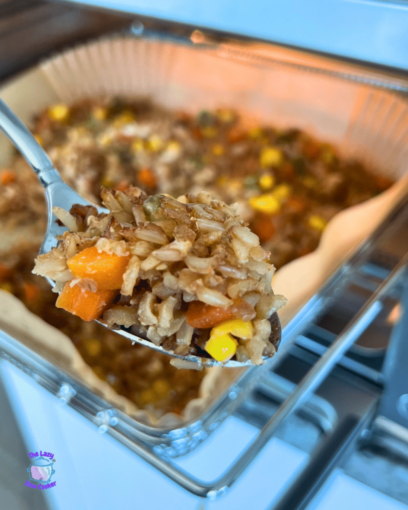 A spoon lifts air fryer fried rice with corn, carrots, and peas above a baking dish of rice inside an oven.
