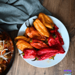 Roasted red and yellow peppers and air-fried baby potatoes served on a white plate, beside cheese-topped food and a blue logo.
