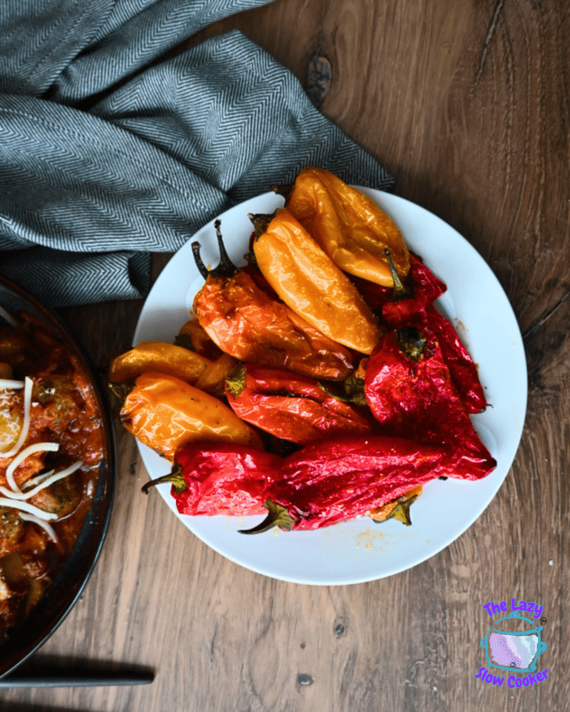Roasted red and yellow peppers and air-fried baby potatoes served on a white plate, beside cheese-topped food and a blue logo.