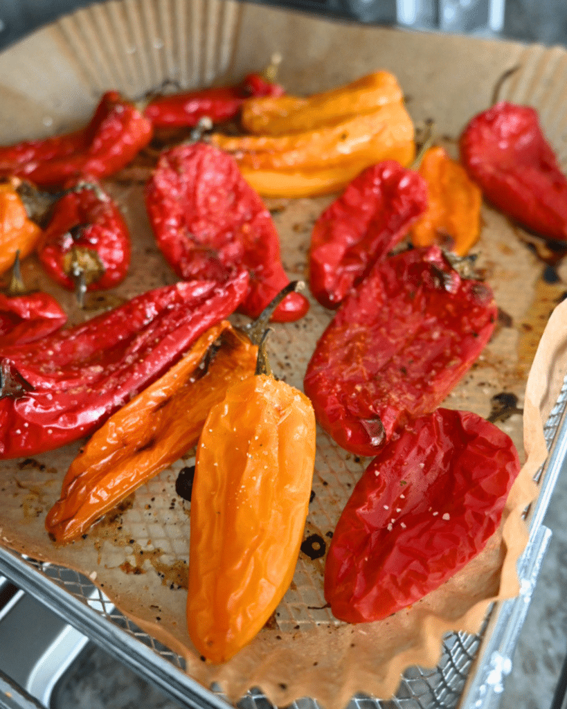 Roasted red and orange peppers with caramelized skin on parchment, next to golden air fryer baby potatoes on a metal oven rack.