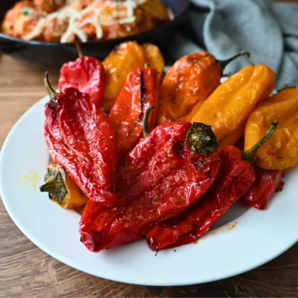 Roasted red and yellow bell peppers on a white plate, with air fryer baby potatoes and a gray napkin on a wooden table nearby.