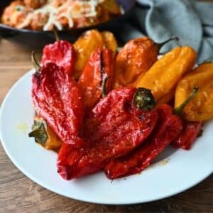 Roasted red and yellow bell peppers on a white plate, with air fryer baby potatoes and a gray napkin on a wooden table nearby.