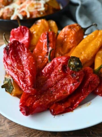 Roasted red and yellow bell peppers on a white plate, with air fryer baby potatoes and a gray napkin on a wooden table nearby.