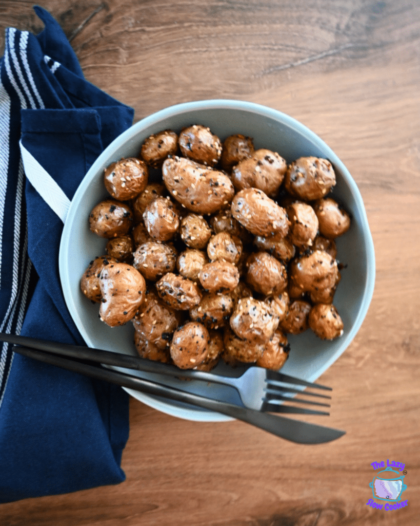 Herbed baby potatoes cooked in an air fryer are served in a bowl on a wooden table with cutlery and a blue-striped napkin nearby.