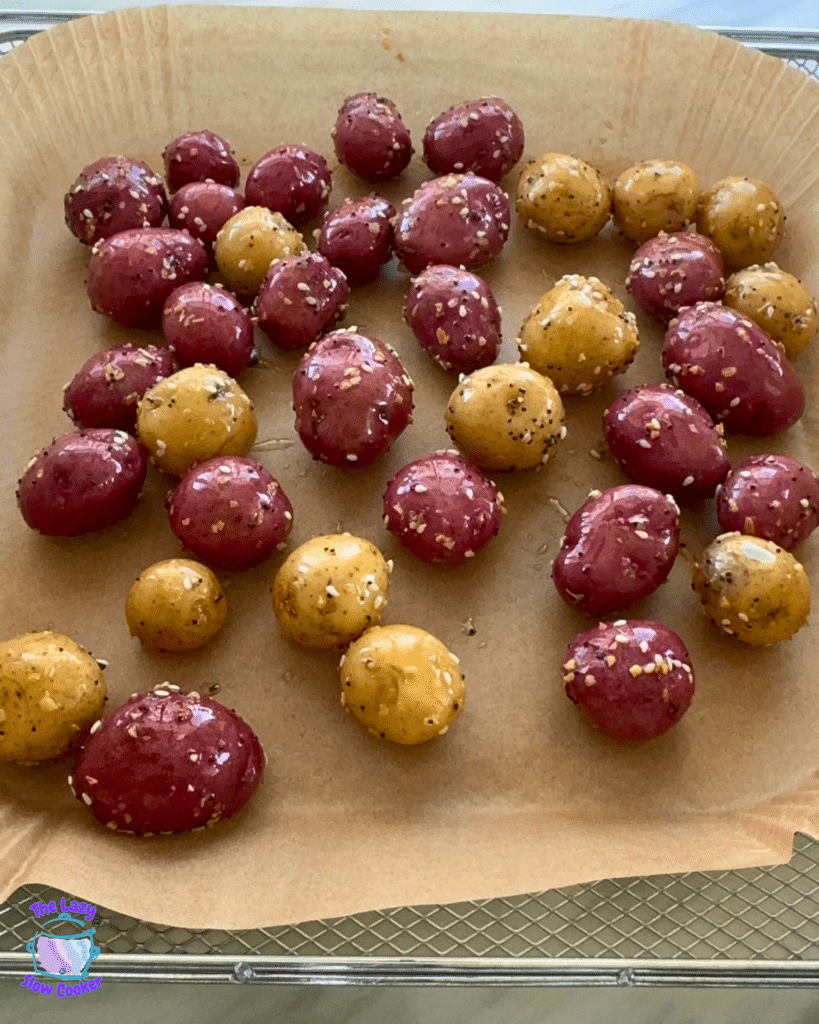 Seasoned red and yellow baby potatoes are spread evenly on a parchment-lined tray, ready for air frying.