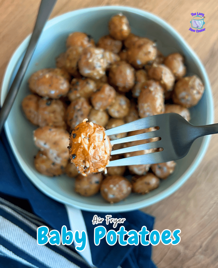 A fork lifts a seasoned air fryer baby potato over a bowl of more potatoes, with a striped napkin