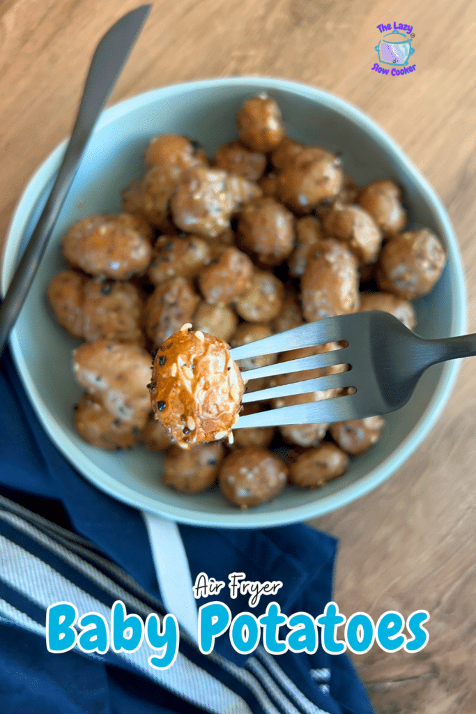 A fork lifts a seasoned air fryer baby potato over a bowl of more potatoes, with a striped napkin