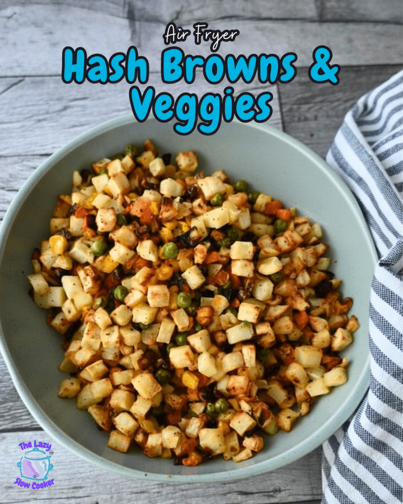 A bowl of golden air-fried hash browns with mixed veggies rests on a wooden table next to a striped cloth. Text: Air Fryer Hash Browns & Veggies.