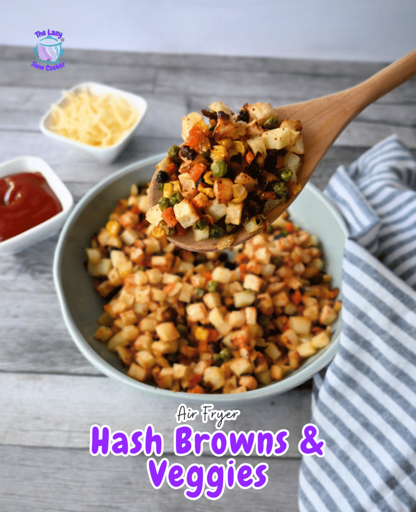 A wooden spoon scoops hash browns and veggies over a bowl, with cheese and ketchup nearby. Text: Air Fryer Hash Browns & Veggies.