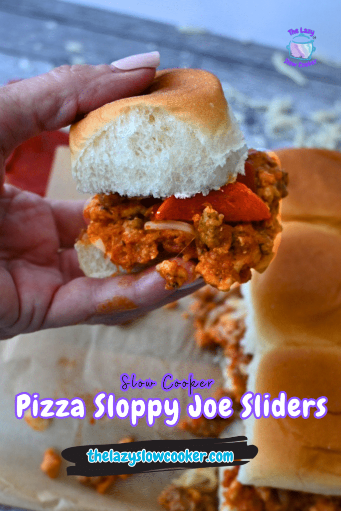 A hand holds a pizza slider filled with saucy meat and pepperoni; more sliders sit on a wooden board. Text: Slow Cooker Pizza Sloppy Joe Sliders thelazyslowcooker.com.