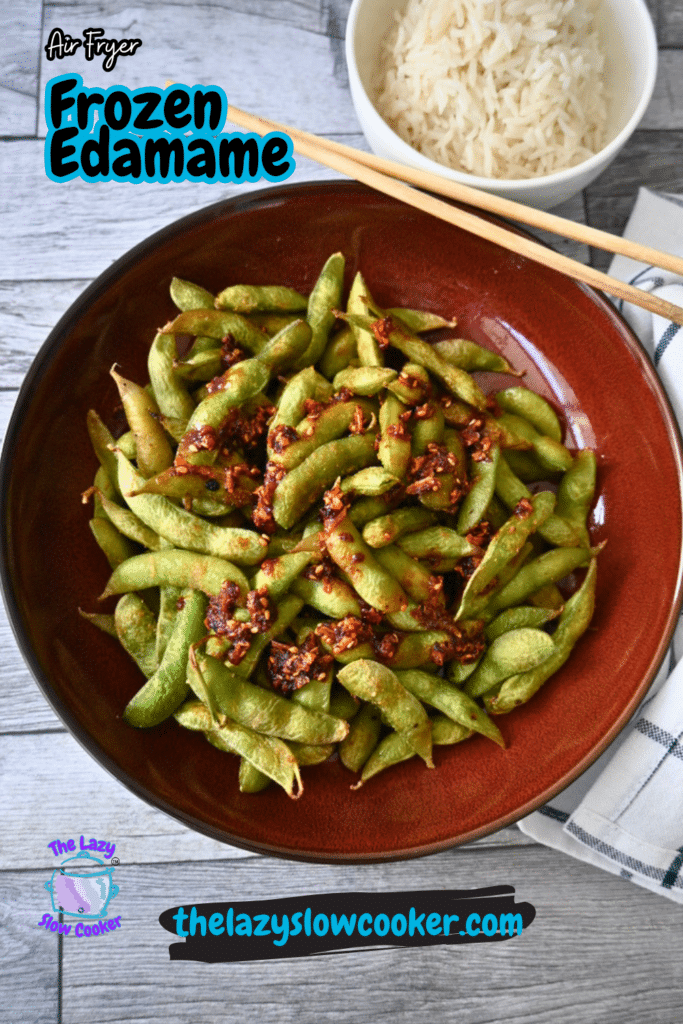 A brown bowl of air-fried frozen edamame with chili flakes sits on wood, next to a rice bowl, chopsticks, and a napkin.