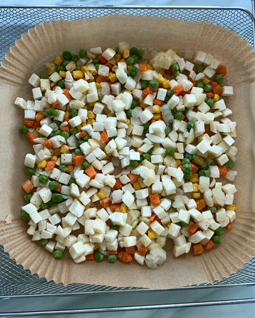 A parchment-lined tray holds diced frozen carrots, peas, corn, and potatoes-ready to go into the air fryer