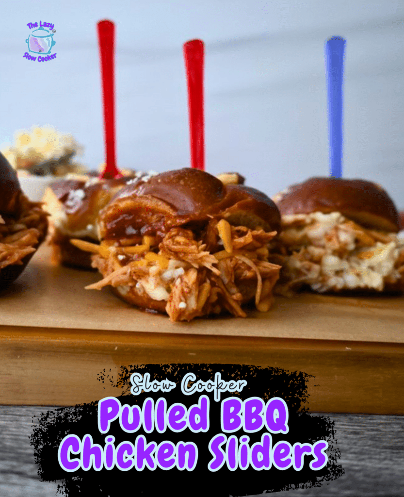 Three pulled BBQ chicken sliders on a wooden board, each with a colorful pick. Text overlay says “Slow Cooker Pulled BBQ Chicken Sliders.”.