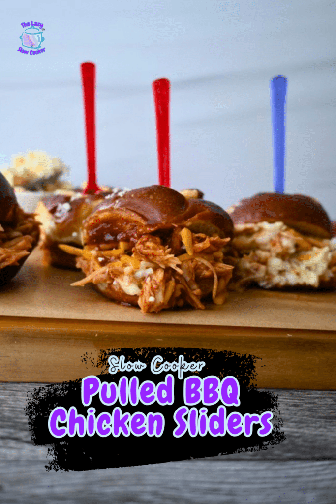 Three pulled BBQ chicken sliders with colorful picks sit on a wooden board. Slow Cooker BBQ Chicken Sliders text above. Mashed potatoes behind.