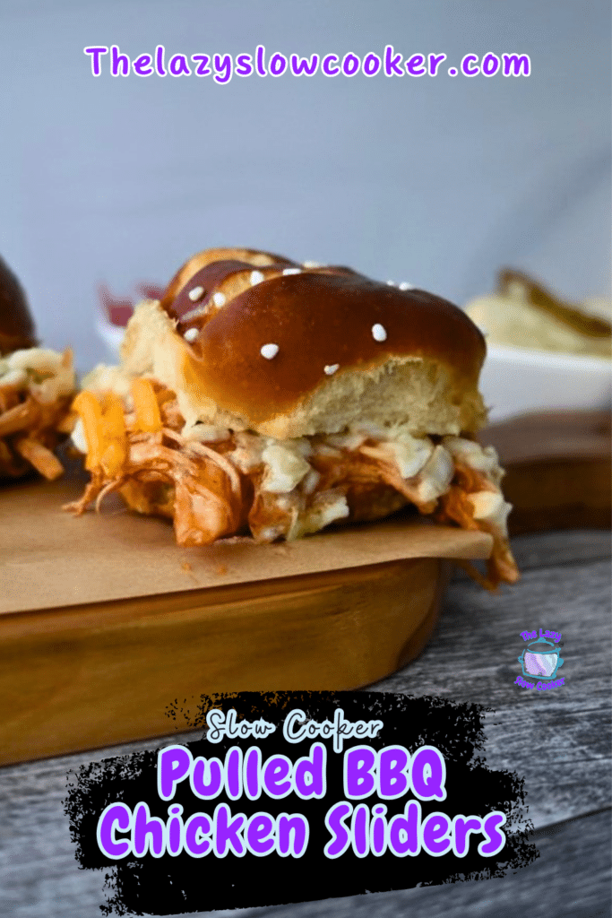 A BBQ chicken slider with shredded cheese on a pretzel bun sits on a wooden board. Text: Slow Cooker BBQ Chicken Sliders.