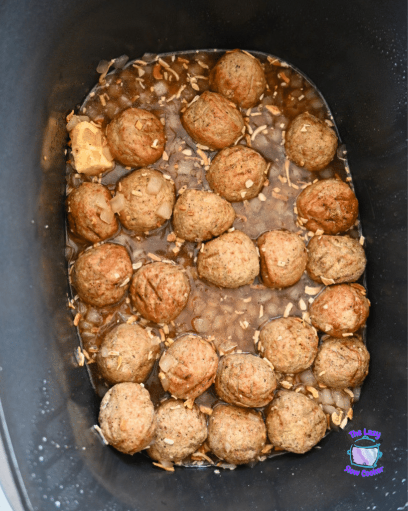 French Onion Meatball Pasta cooks in a slow cooker, with meatballs, chopped onions, broth, and a pat of butter melting on the side.