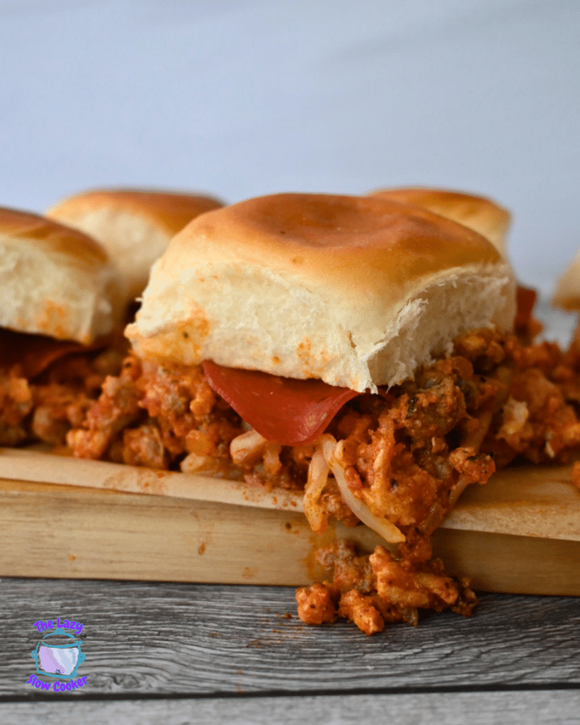 Three golden brown buns filled with ground meat, cheese, and pepperoni sit on a wooden board, filling spilling out the sides.
