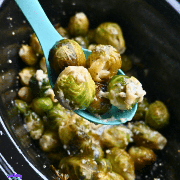 A turquoise spoon lifts cheesy, seasoned Brussels sprouts from a pot of more Brussels sprouts cooked in a slow cooker.
