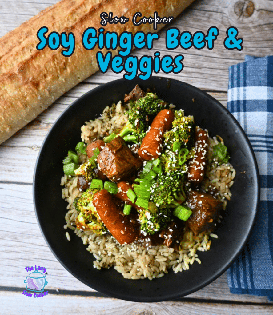 A black bowl with soy ginger beef, carrots, broccoli, and rice sits on a wooden table next to a baguette and plaid napkin. Text: Slow Cooker Soy Ginger Beef & Veggies.