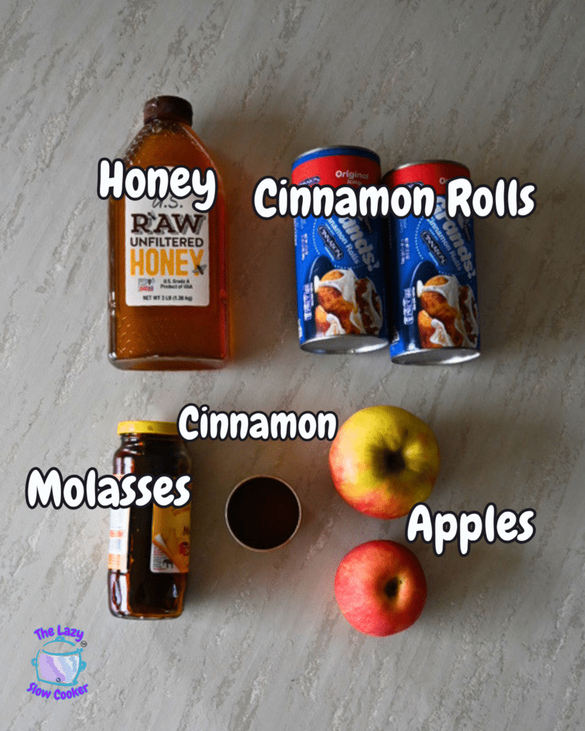 An overhead shot shows honey, two apples, ground cinnamon in a small bowl, molasses, and two cans of cinnamon rolls arranged on a light-colored surface. Each ingredient is labeled in bold white text. These are the main ingredients for making slow cooker apple monkey bread.