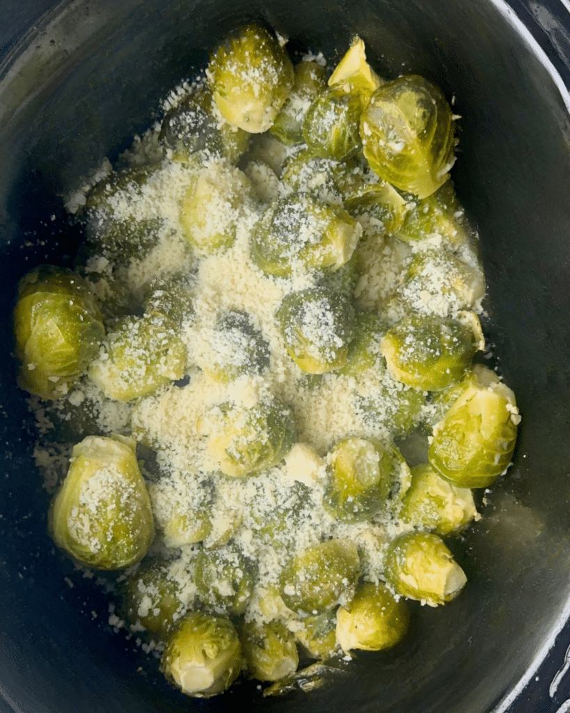 A pot of brussels sprouts in a slow cooker is topped with grated parmesan cheese, prepared and ready for cooking or serving.