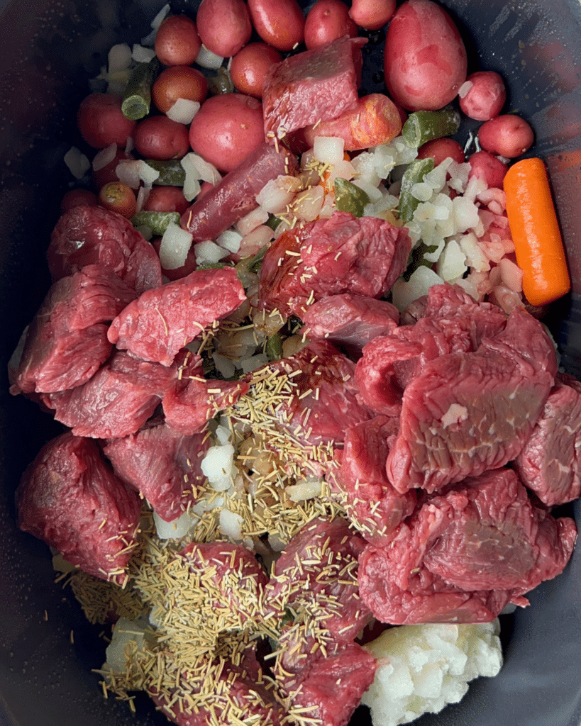 Raw beef, potatoes, carrots, onions, and green beans layered with herbs in a slow cooker to make garlic herb beef stew.
