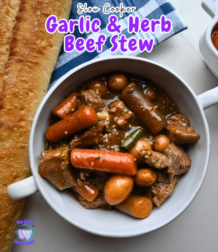 A bowl of garlic herb beef stew with carrots and potatoes is on a white table beside a baguette. Purple text above names the dish.