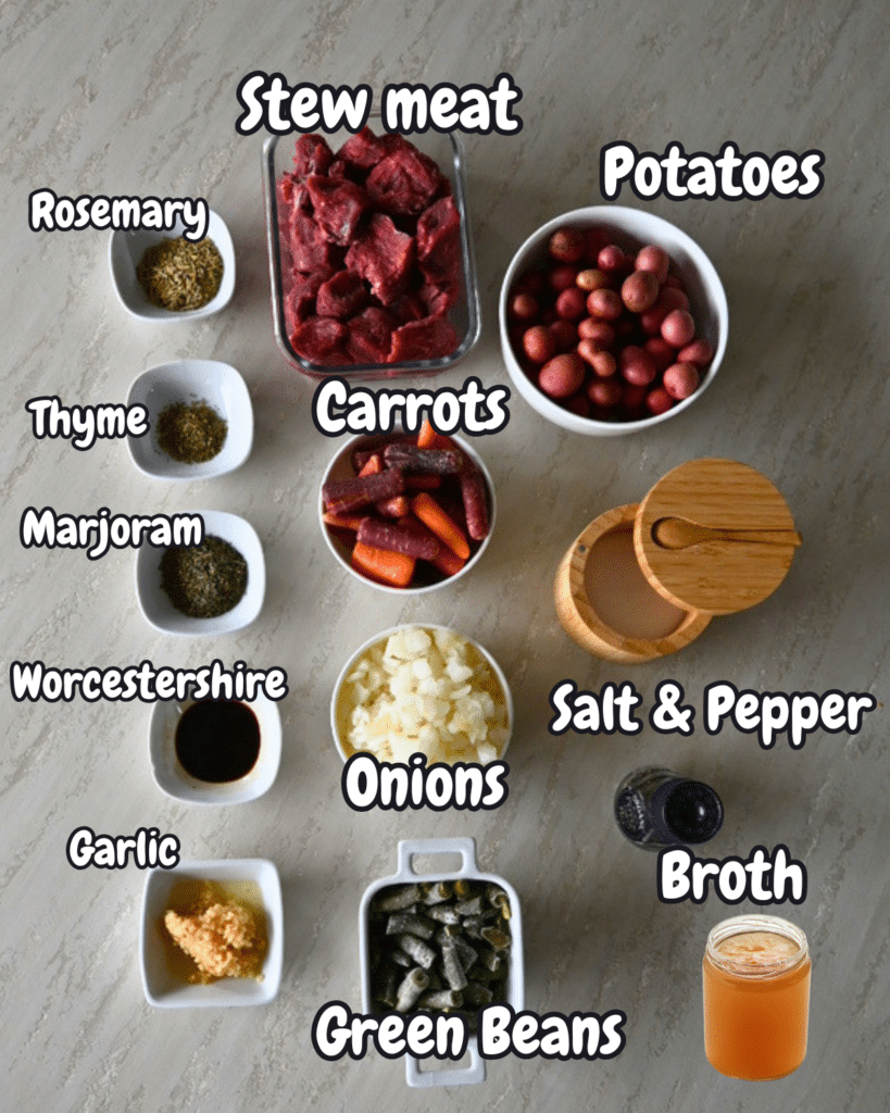 Ingredients for slow cooker garlic herb beef stew are arranged on a surface, each labeled, including meat, veggies, herbs, and broth.