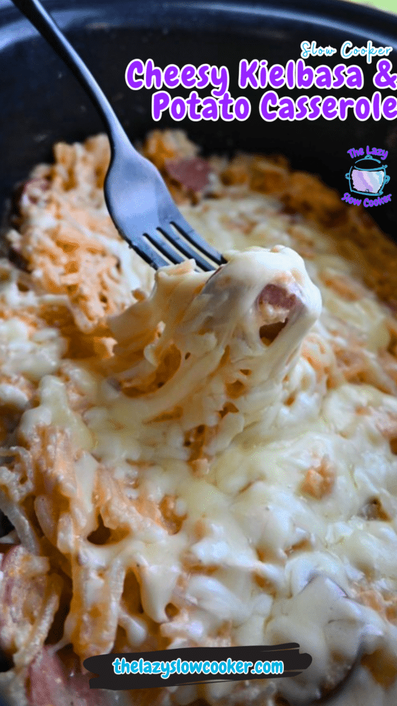 A fork lifts a cheesy bite of slow cooker kielbasa and potato casserole, with melted cheese stretching. The text reads the recipe name.