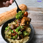 A hand holds a fork with soy ginger beef, broccoli, and veggies over a rice bowl. A baguette and The Lazy Slow Cooker logo are visible.