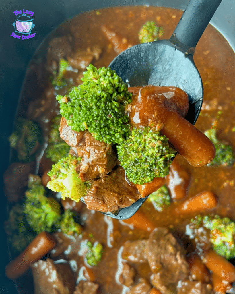 A spoon lifts tender soy ginger beef, broccoli, and carrots from a hearty slow cooker stew; The Lazy Slow Cooker logo appears above.