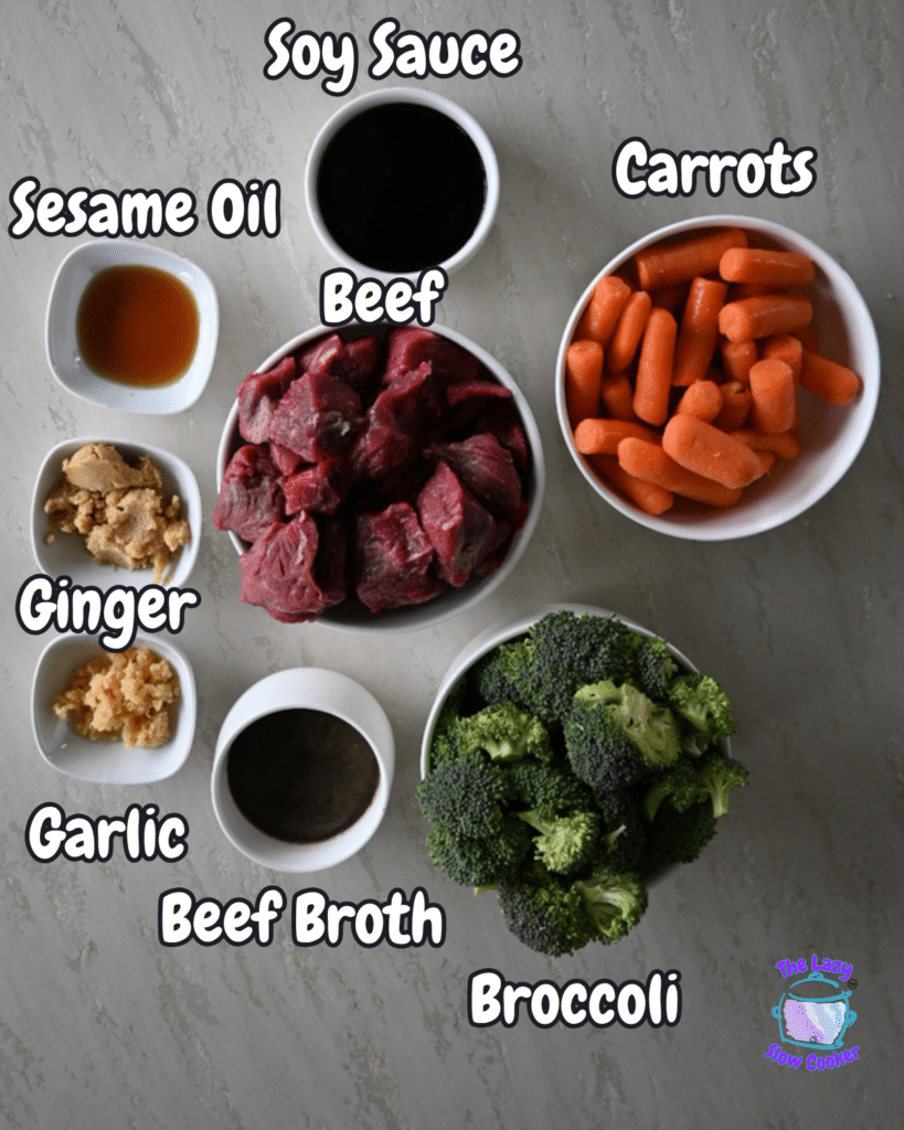Ingredients for slow cooker soy ginger beef are arranged in bowls on a marble counter, each labeled: beef, veggies, sauces, and seasonings.