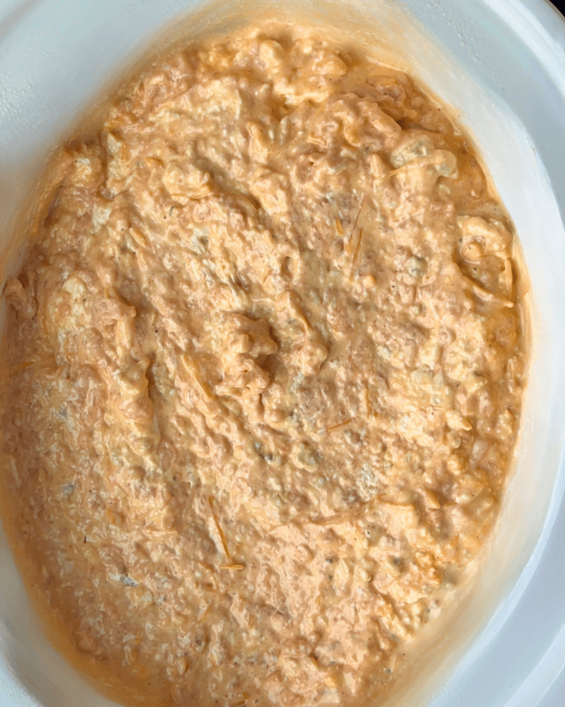 A close-up of creamy, orange buffalo dip made with ground chicken, topped with melted shredded cheese and sprinkled with chopped green herbs, served in a white bowl.