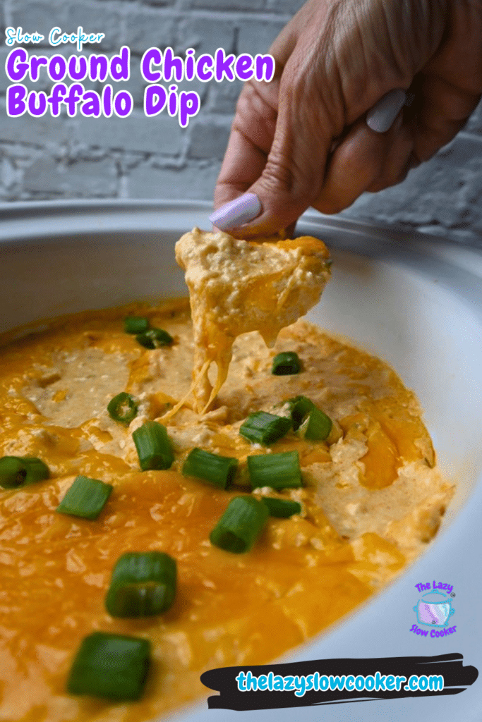 A person dips a chip into a creamy, orange buffalo chicken dip with melted cheese and sliced green onions in a slow cooker. The image includes the text: Slow Cooker Ground Chicken Buffalo Dip.