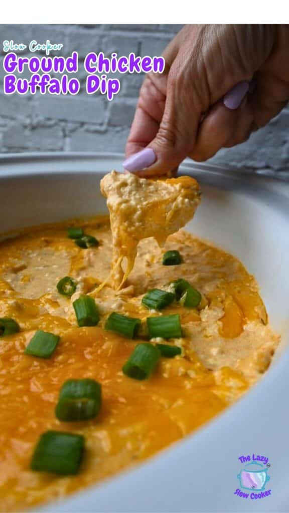 A person dips a chip into a creamy buffalo dip made with ground chicken and topped with chopped green onions, served in a white slow cooker. The words “Slow Cooker Ground Chicken Buffalo Dip” appear on the image.