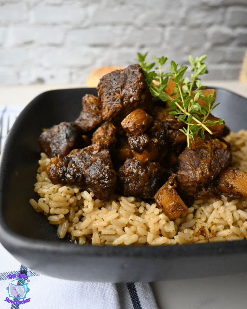 A black bowl holds a serving of seasoned rice topped with pieces of honey balsamic beef and roasted butternut squash, finished with a few fresh thyme sprigs.