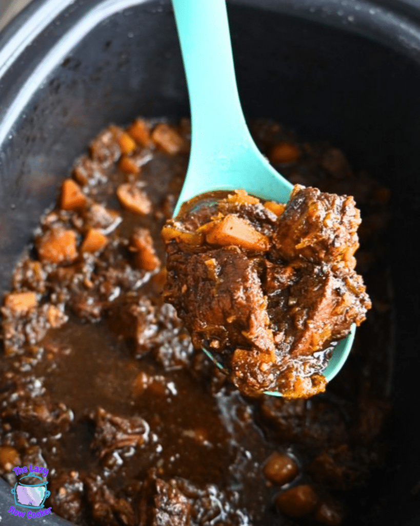A teal spoon lifts a serving of honey balsamic beef and butternut squash stew from a pot, showing pieces of beef, orange squash, carrots, and thick brown gravy.