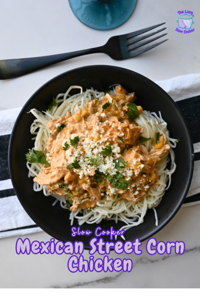 A black bowl filled with spaghetti and Mexican Street Corn Chicken from a slow cooker, topped with cilantro and cheese, rests on a striped napkin next to a fork. The image includes the text: Slow Cooker Mexican Street Corn Chicken.