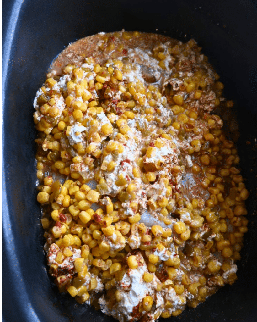 A slow cooker filled with a creamy mixture of corn, cream cheese, and spices. The ingredients are smoothly blended and partially melted, resembling a rich dip or casserole inspired by Mexican street corn chicken.