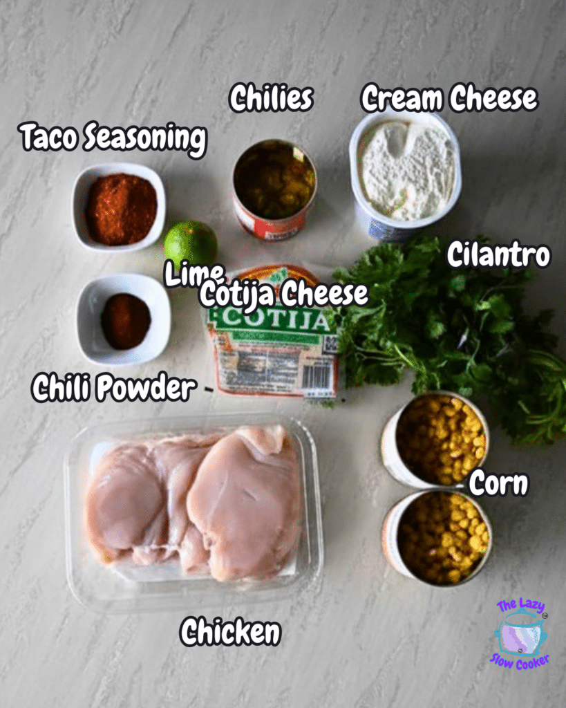 A top-down view shows the ingredients for Slow Cooker Mexican Street Corn Chicken neatly arranged on a table, including raw chicken breasts, corn, chili powder, Cotija cheese, lime, cilantro, cream cheese, chilies, and taco seasoning. Each ingredient has a clear label.
