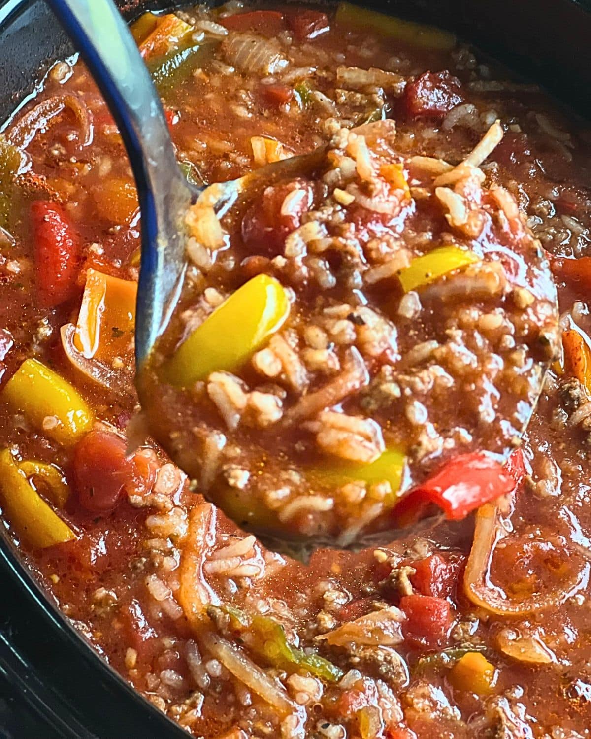 A close-up view shows a ladle lifting stuffed pepper soup made with ground meat, rice, bell peppers, and tomatoes from a pot.