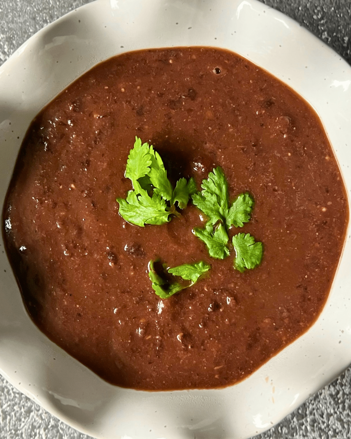 A white bowl filled with black bean soup topped with fresh cilantro sits on a gray surface, showing the finished result of a slow-cooked recipe.