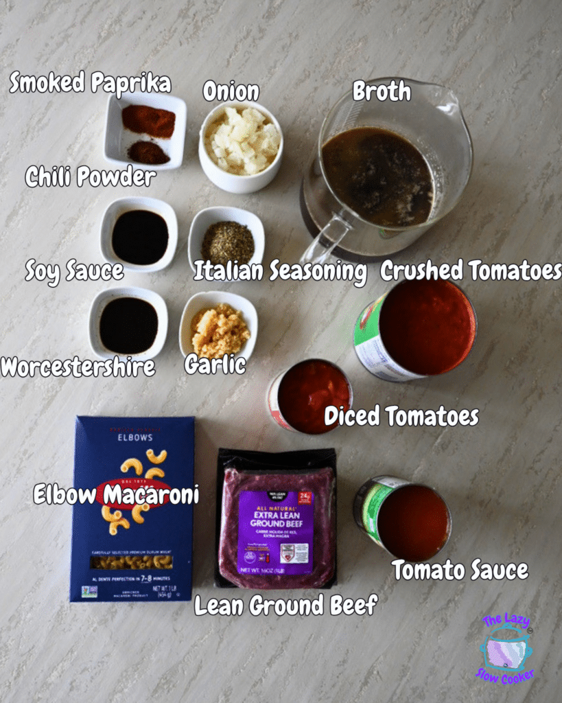 All the ingredients for slow cooker American goulash are neatly laid out on a kitchen counter, including small bowls of seasonings, chopped onion, broth, soy sauce, Worcestershire sauce, minced garlic, dry elbow macaroni, raw ground beef, and open cans of crushed tomatoes, diced tomatoes, and tomato sauce.